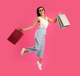 Photo of Beautiful young woman with paper shopping bags jumping on pink background