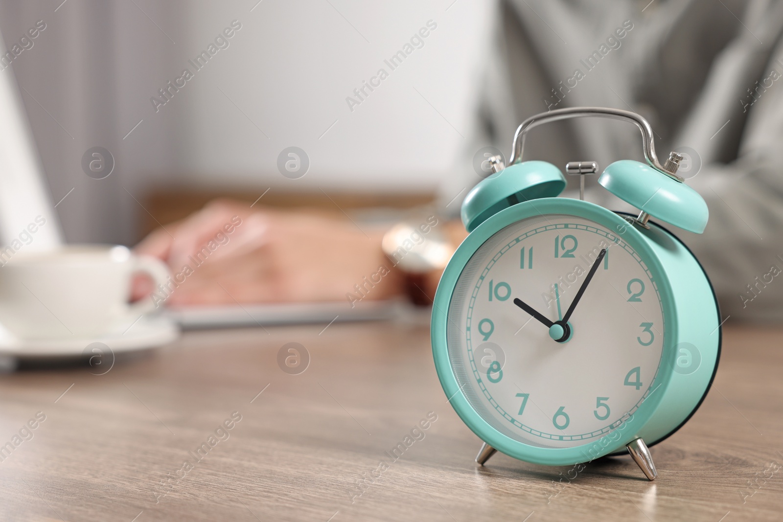 Photo of Turquoise alarm clock and man working at table in office, closeup with space for text. Deadline concept