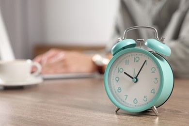 Photo of Turquoise alarm clock and man working at table in office, closeup with space for text. Deadline concept