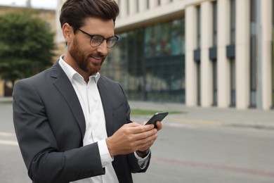 Handsome businessman with smartphone on city street, space for text