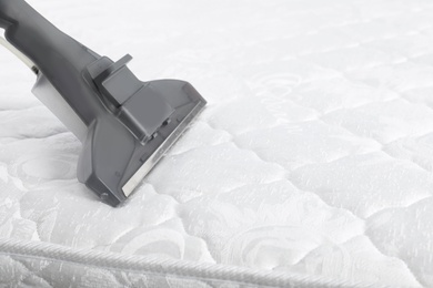 Photo of Using modern vacuum cleaner for mattress disinfection, closeup. Space for text