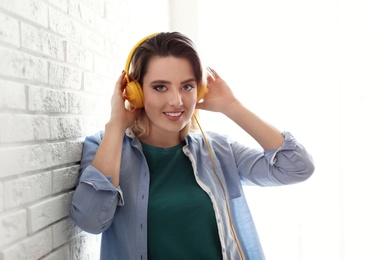 Photo of Portrait of beautiful woman listening to music with headphones near brick wall