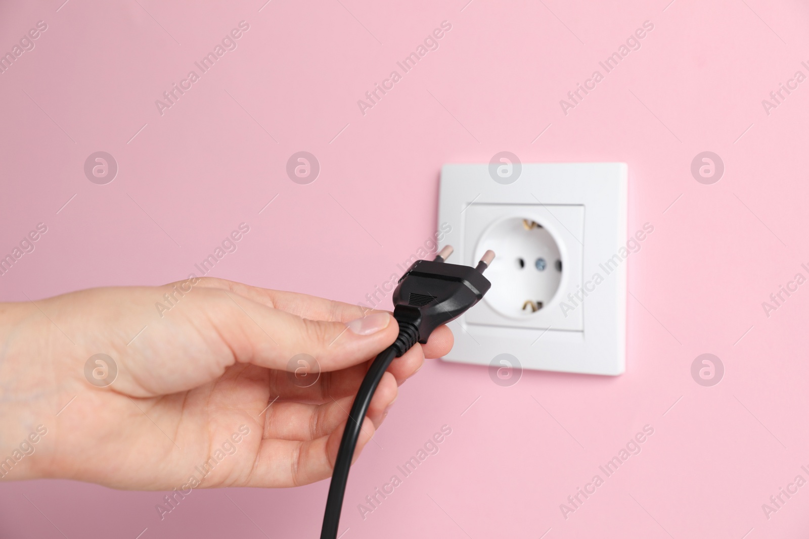 Photo of Woman inserting plug into power socket on pink wall, closeup. Electrical supply