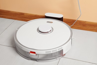 Photo of Modern robotic vacuum cleaner charging on white floor indoors, closeup