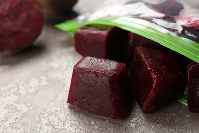 Photo of Frozen beet puree cubes in plastic bag on marble table, closeup