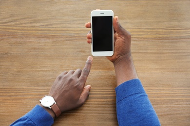 Photo of African-American man holding mobile phone with blank screen in hand at table