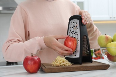 Woman grating fresh red apple at kitchen table, closeup