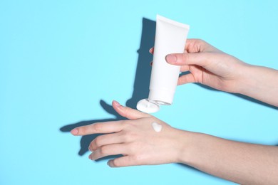 Woman with tube applying cream on her hand against light blue background, closeup