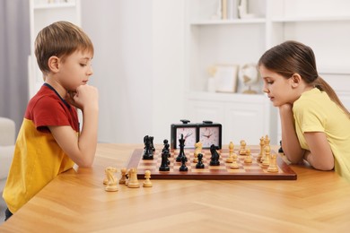 Photo of Cute children playing chess at table in room