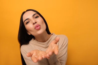 Beautiful young woman taking selfie while blowing kiss on orange background. Space for text