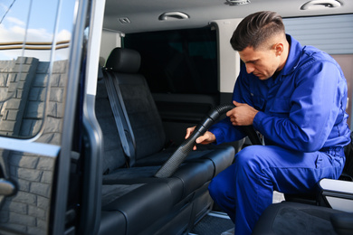 Photo of Car wash worker vacuuming upholstery on automobile seat