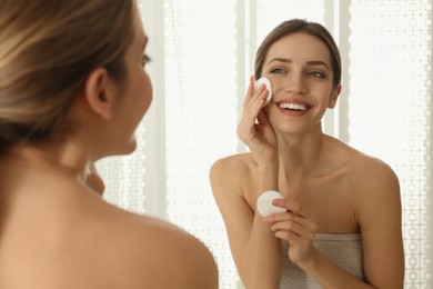 Photo of Young woman with cotton pads cleaning her face near mirror in bathroom