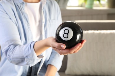 Photo of Woman holding magic eight ball indoors, closeup