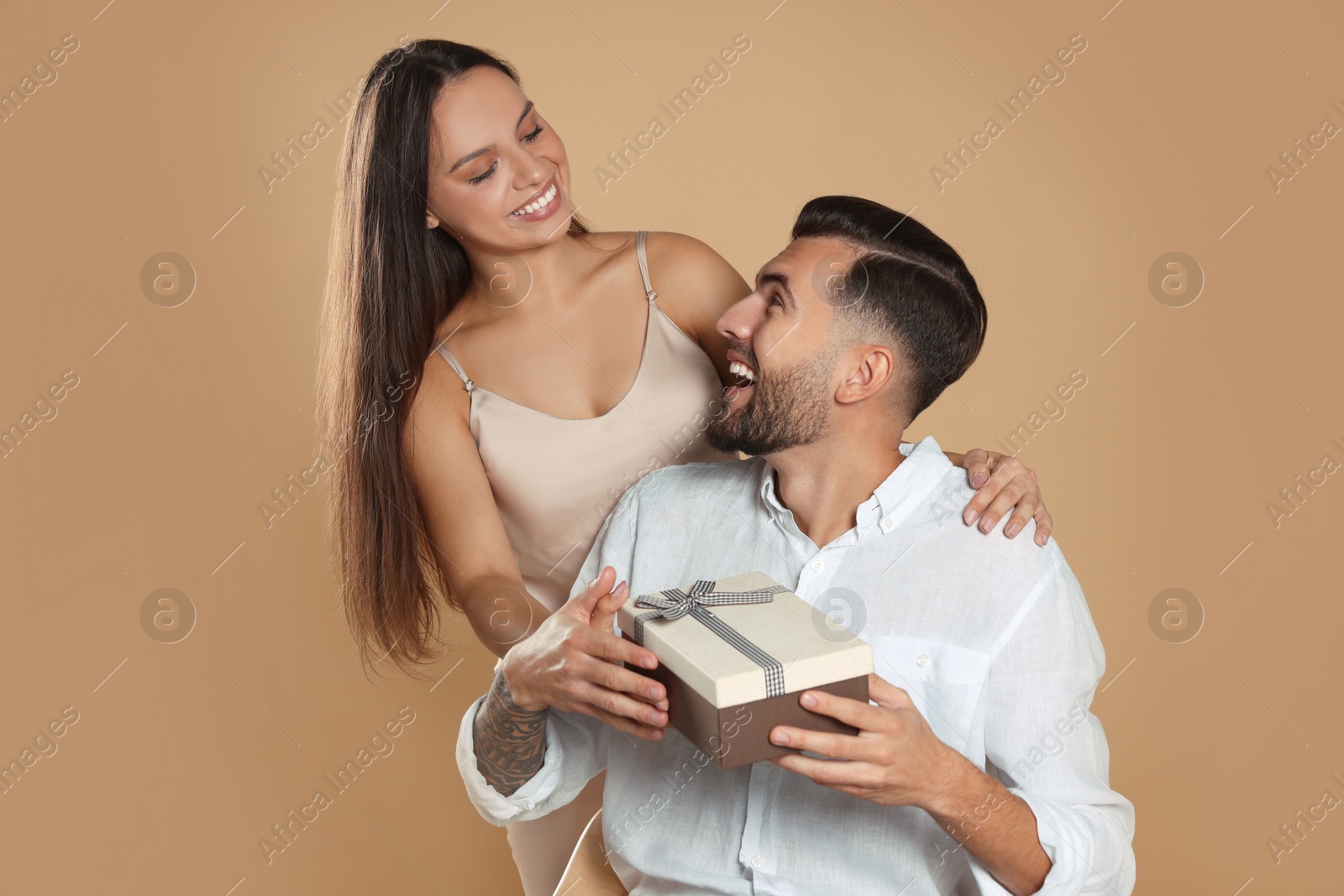 Photo of Woman presenting gift to her boyfriend on beige background