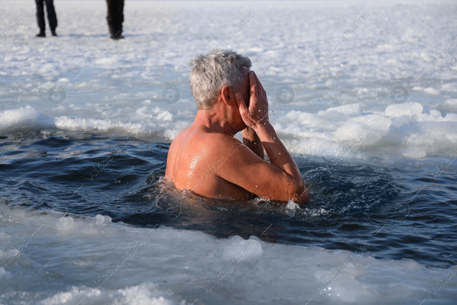 Photo of MYKOLAIV, UKRAINE - JANUARY 06, 2021: Mature man immersing in icy water on winter day