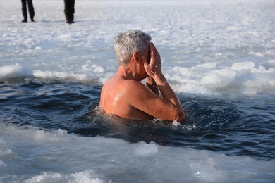 MYKOLAIV, UKRAINE - JANUARY 06, 2021: Mature man immersing in icy water on winter day