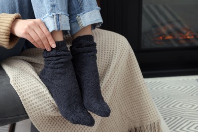 Photo of Woman in warm socks relaxing near fireplace at home, closeup
