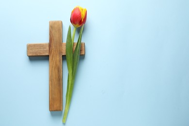Easter - celebration of Jesus resurrection. Wooden cross and tulip on light blue background, top view. Space for text