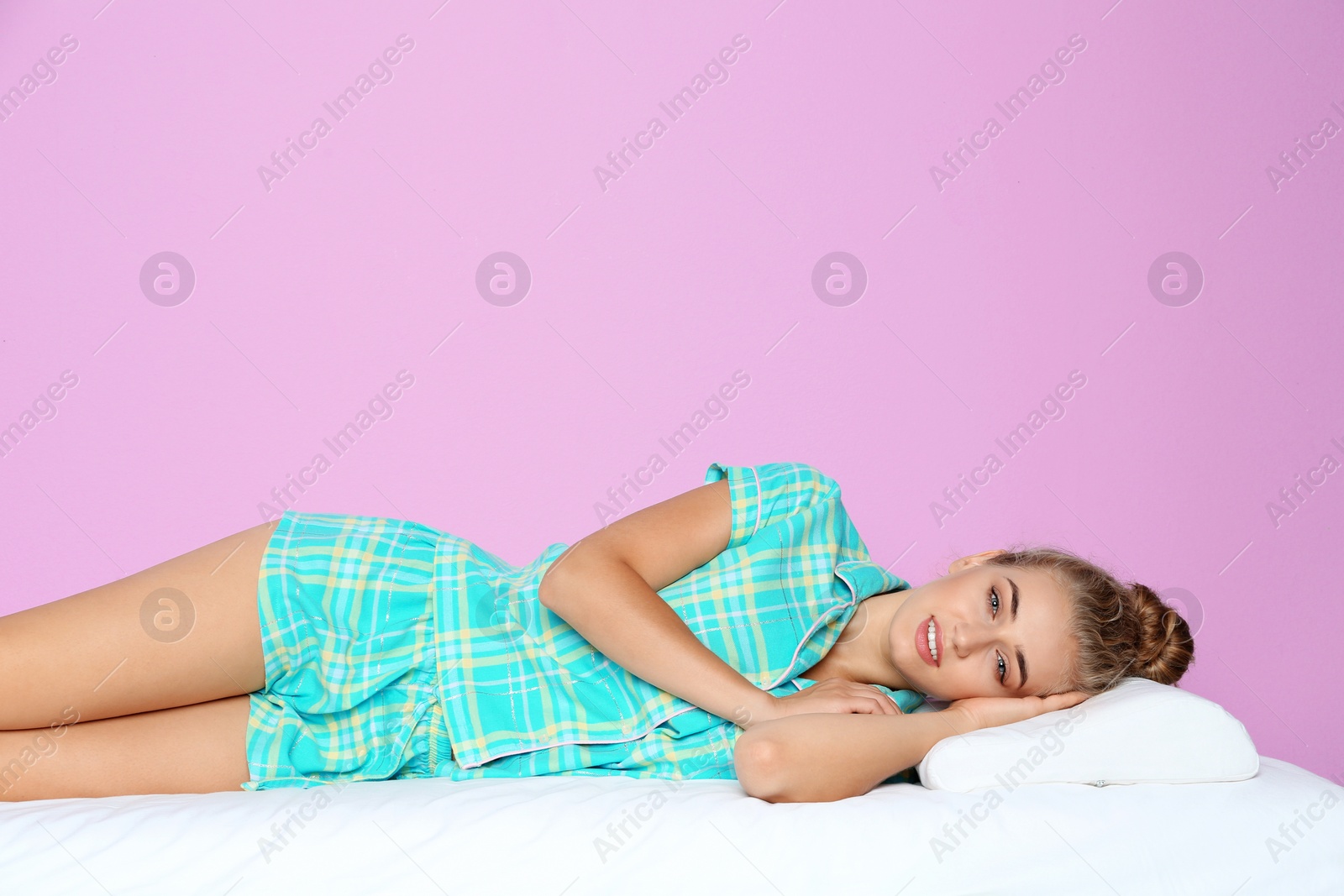 Photo of Beautiful woman lying with orthopedic pillow on bed against color background