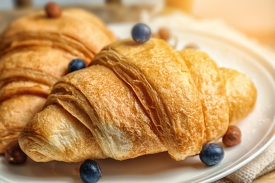 Tasty croissant with berries and nuts on plate, closeup