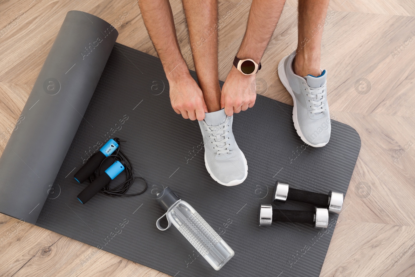 Photo of Top view of man putting on sneakers, yoga mat, bottle, skipping rope and dumbbells