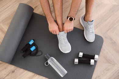 Top view of man putting on sneakers, yoga mat, bottle, skipping rope and dumbbells