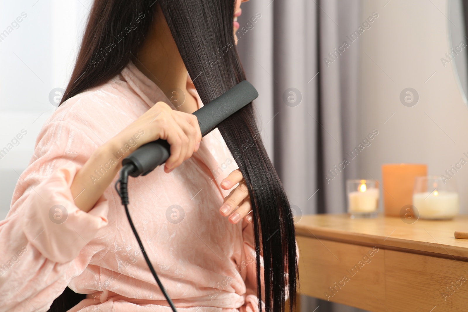 Photo of Woman using hair iron in room, closeup. Space for text