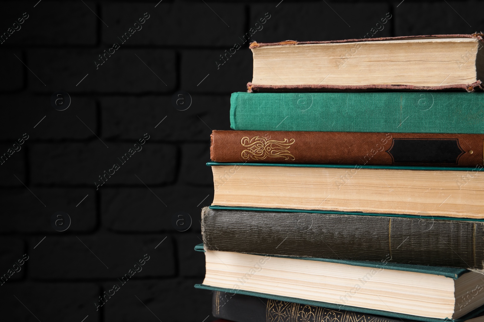 Photo of Many old hardcover books near black brick wall, closeup. Space for text