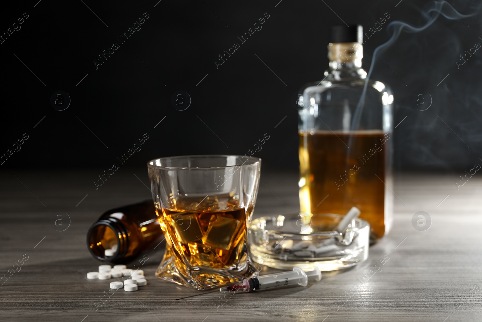 Photo of Alcohol and drug addiction. Whiskey in glass, syringe, pills and cigarettes on wooden table