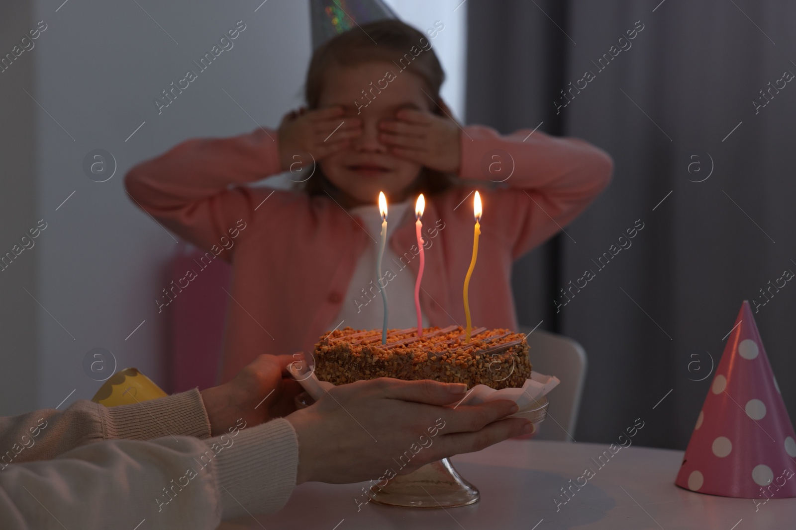 Photo of Birthday celebration. Mother holding tasty cake near her daughter indoors, focus on burning candles