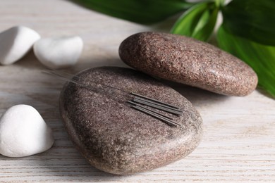 Photo of Stones with acupuncture needles on white wooden table