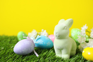 Photo of Easter bunny toy and dyed eggs on green grass against yellow background. Space for text