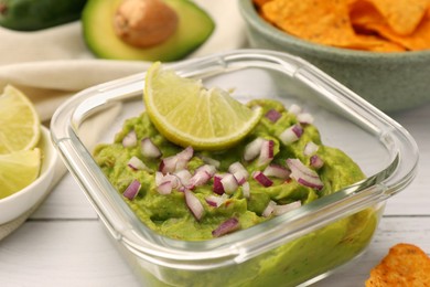Photo of Bowl of delicious guacamole with onion and lime on white wooden table, closeup
