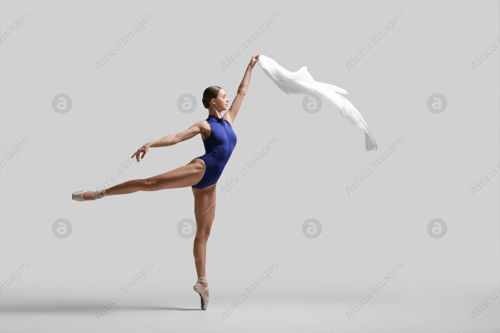 Photo of Graceful young ballerina practicing dance moves with veil on light grey background