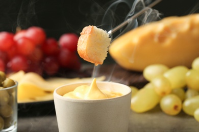 Photo of Piece of bread over bowl with delicious cheese fondue, closeup