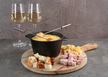 Fondue pot with tasty melted cheese, forks, wine and different snacks on grey table