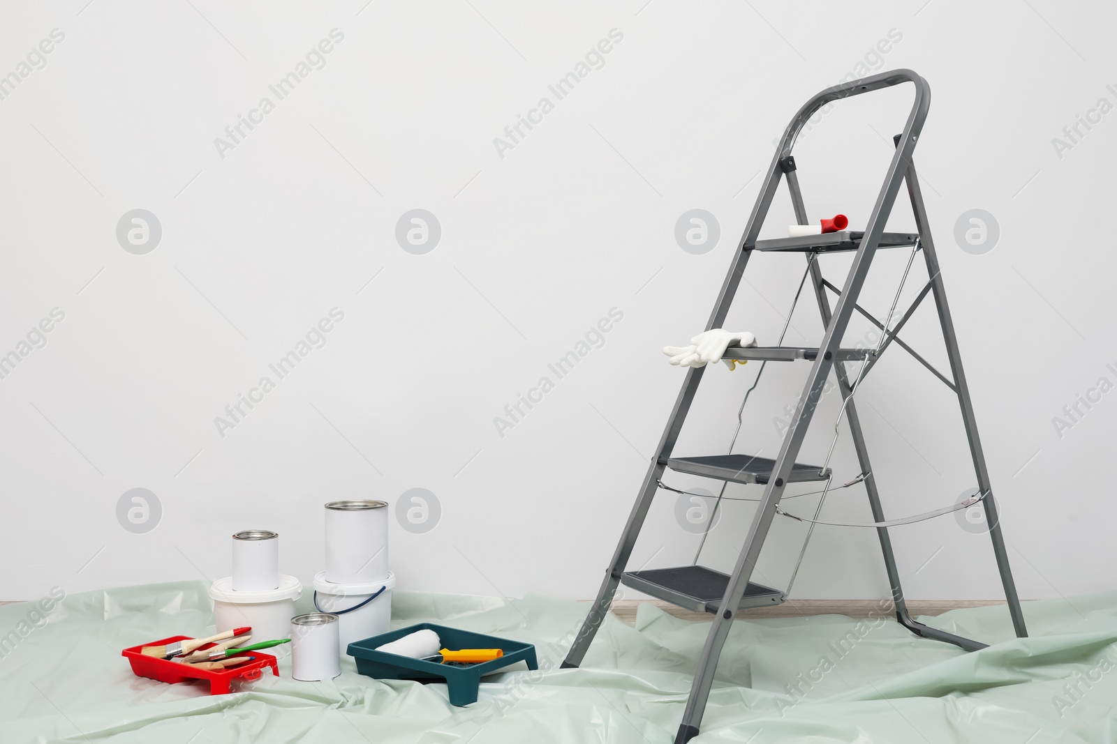 Photo of Metallic folding ladder and painting tools indoors, space for text