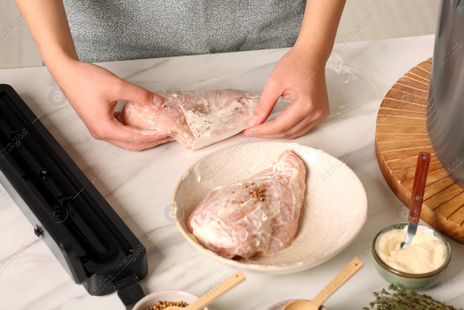 Photo of Woman putting meat into plastic bag on table in kitchen, closeup. Sealer for vacuum packing