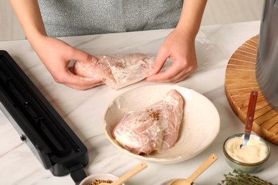 Photo of Woman putting meat into plastic bag on table in kitchen, closeup. Sealer for vacuum packing