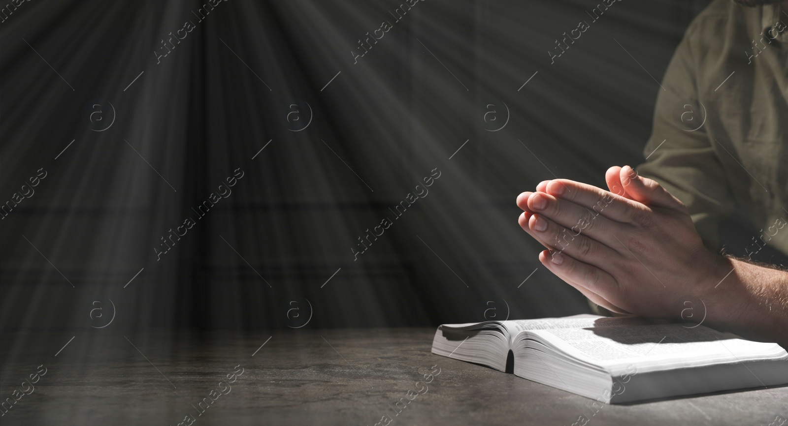 Image of Religion. Christian man praying over Bible at table, closeup. Banner design