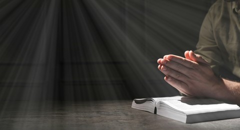 Religion. Christian man praying over Bible at table, closeup. Banner design