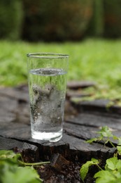 Glass of fresh water on wooden stump in green grass outdoors