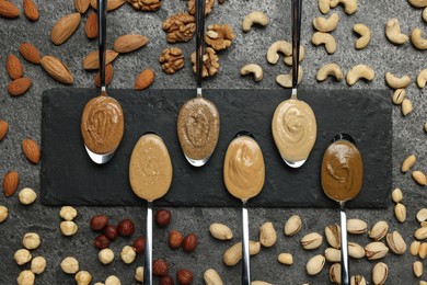 Tasty nut butters in spoons and raw nuts on gray table, flat lay