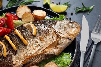 Photo of Tasty homemade roasted crucian carp served on black table, closeup. River fish