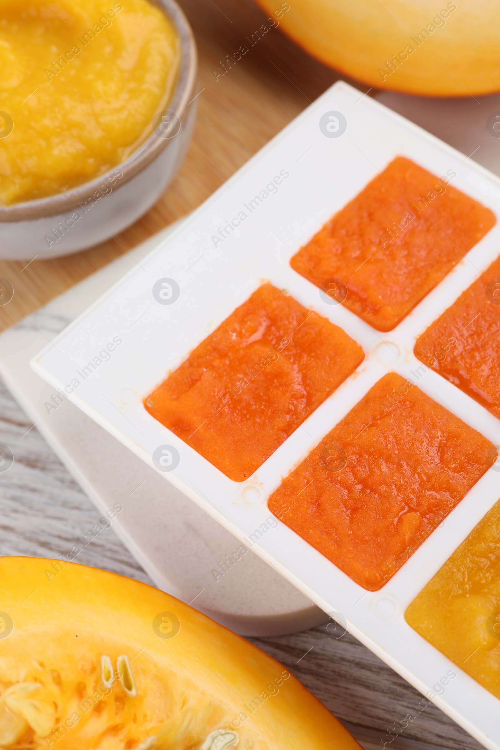 Photo of Different purees in ice cube tray ready for freezing on table, closeup