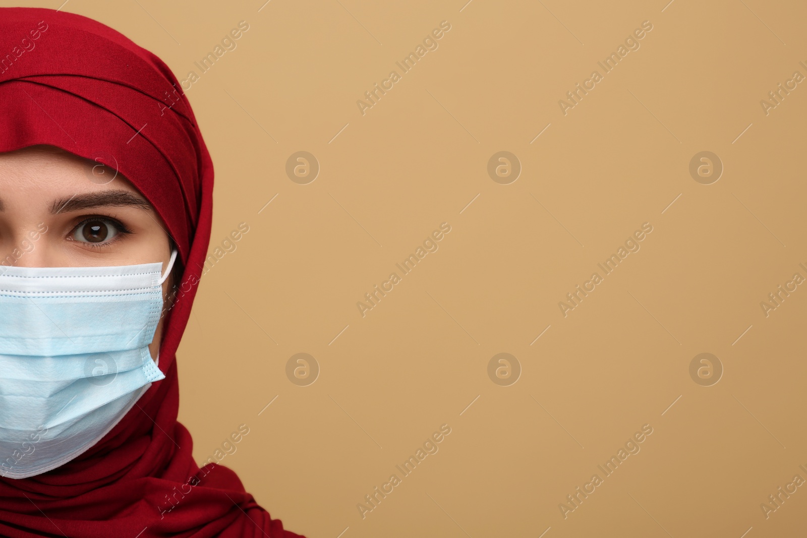 Photo of Muslim woman in hijab and medical mask on beige background, space for text
