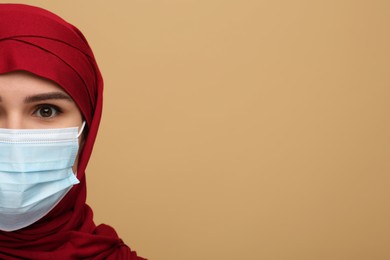 Muslim woman in hijab and medical mask on beige background, space for text