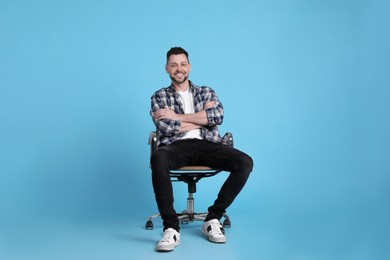 Handsome man sitting in office chair on light blue background