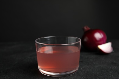 Photo of Glass of onion syrup and fresh vegetable on dark table