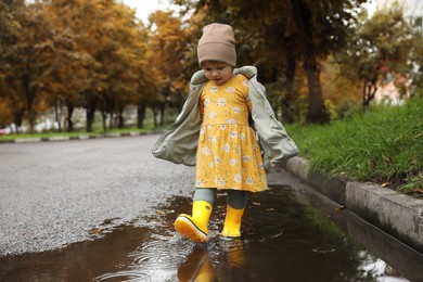Photo of Cute little girl splashing water with her boots in puddle outdoors